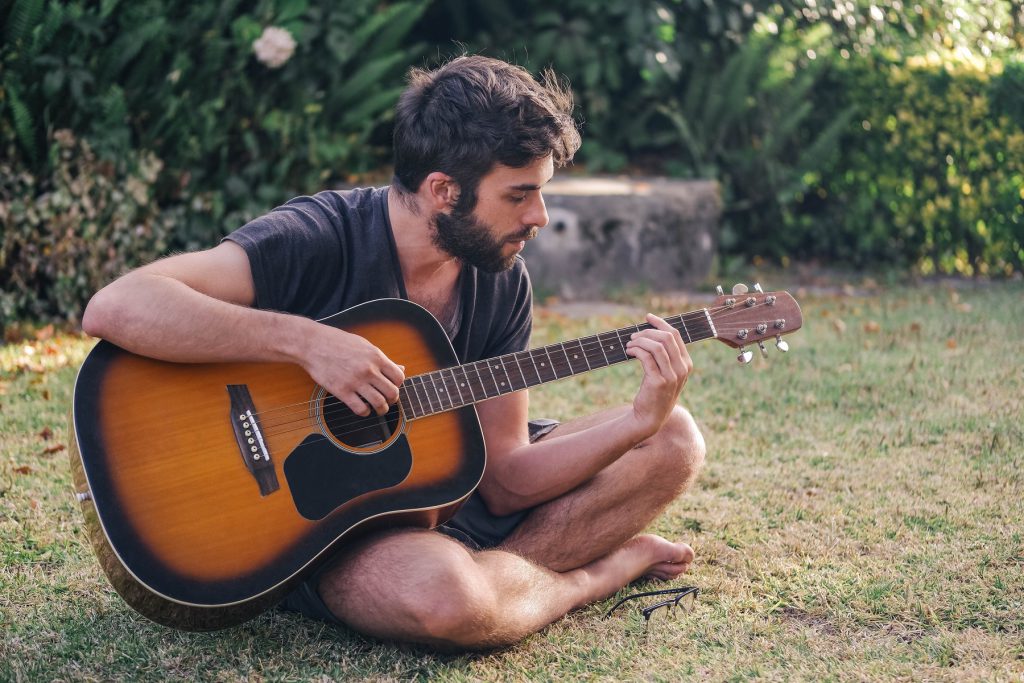 Mężczyzna grający na gitarze akustycznej na trawie