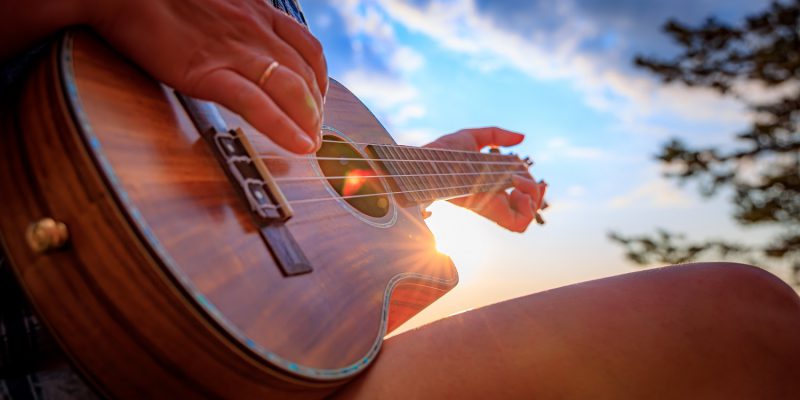 Osoba grająca na ukulele o zachodzie słońca