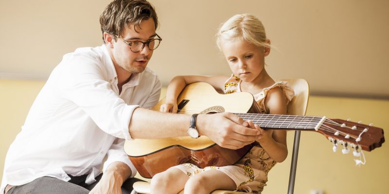Mężczyzna uczący dziewczynkę gry na gitarze