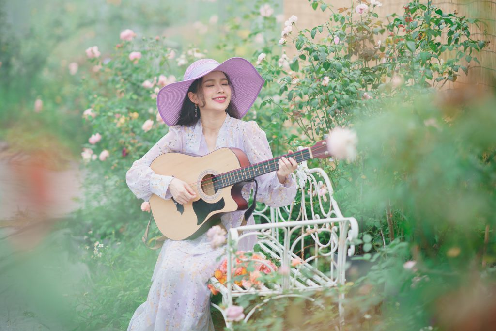Kobieta w kapeluszu grająca na gitarze pośród kwiatów