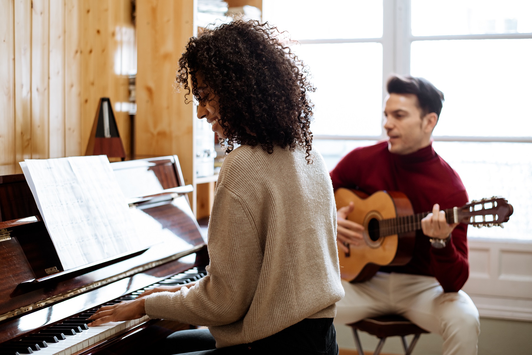 Woman playing piano near man playing guitar in studio